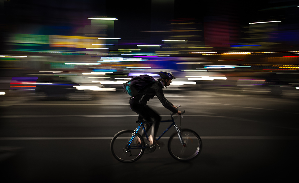 Ein Fahrradfahrer mit dunkler Kleidung und dunklem Rad fährt offensichtlich schnell durch die Dunkelheit