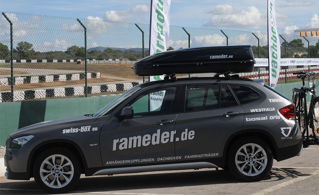 Graues Auto mit Rameder.de-Schriftzug und Dachbox