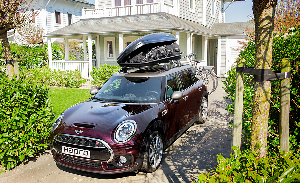 Ein roter Mini Cooper mit geöffneter Dachbox und Fahrradträger auf der Anhängerkupplung und montierten Fahrrädern