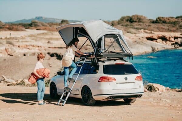 Zwei Frauen mit einem weißen VW Kombi mit Dachzelt Lady Tend an der Küste eines Sees