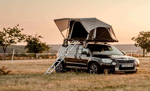 Schwarzer SUV mit montiertem Dachzelt auf einer Pferdekoppel bei Sonnenuntergang
