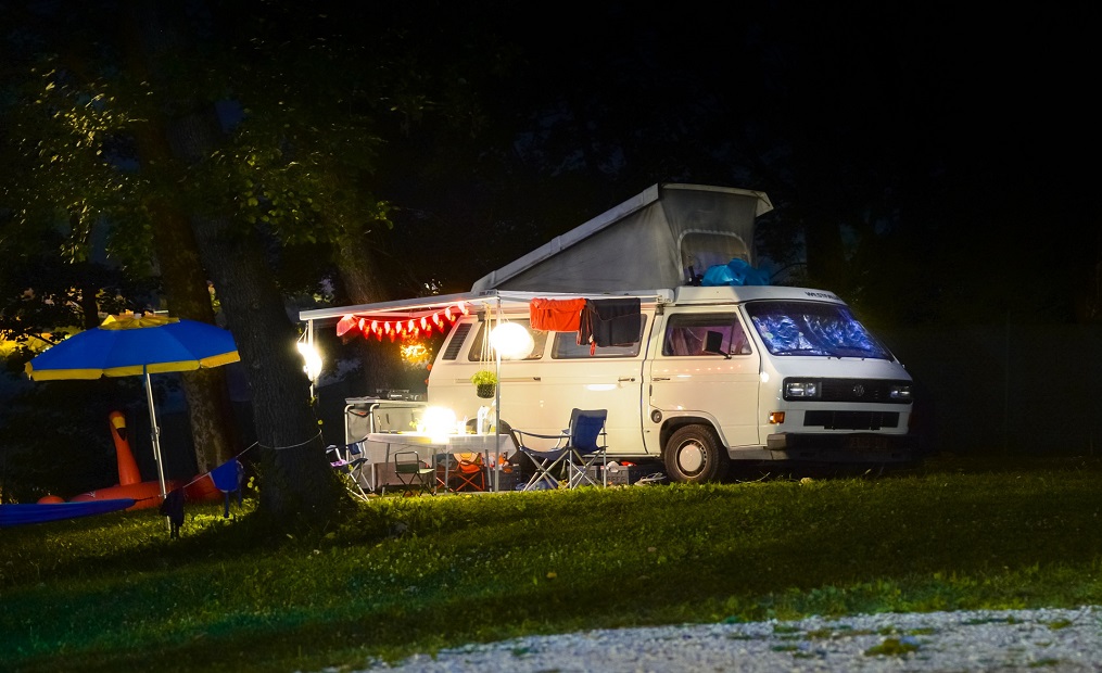 VW T3-Bus mit Hochstellt-Dachzelt, Markise, Sitzgruppe und Beleuchtung im Dunkeln