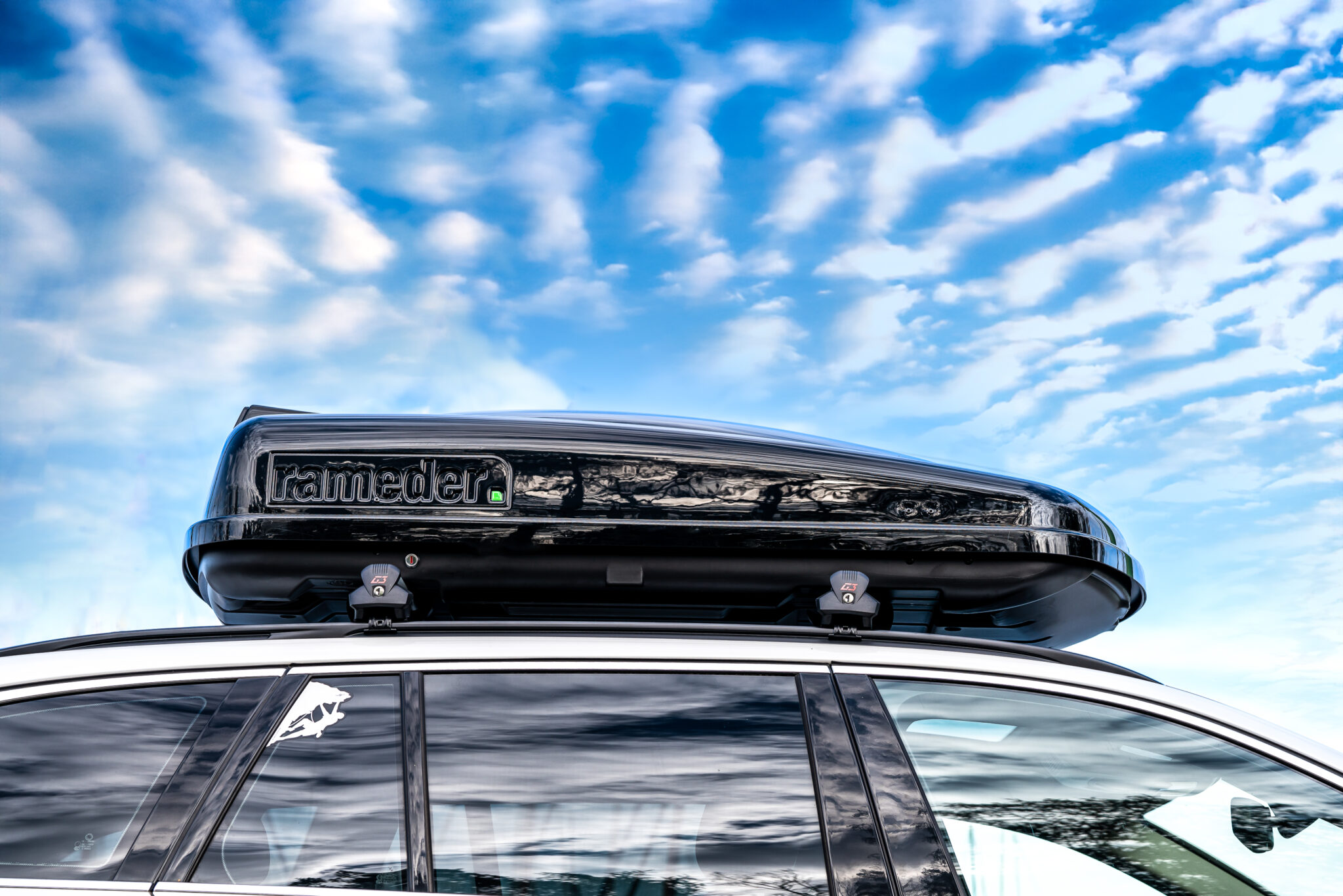 auf einem Autodach montierte schwarze Dachbox und blauer Himmel mit kleinen Wölkchen im Hintergrund